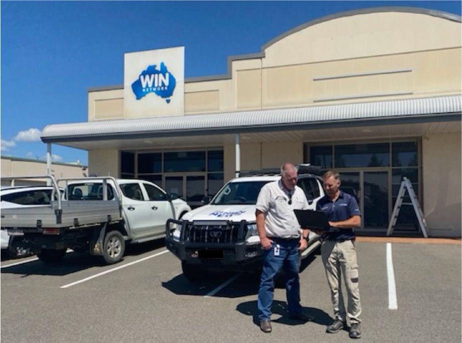 Two men, one from AirBridge Network and one from Nine News, having a conversation in front of the Nine News office, with a branded vehicle parked nearby.
