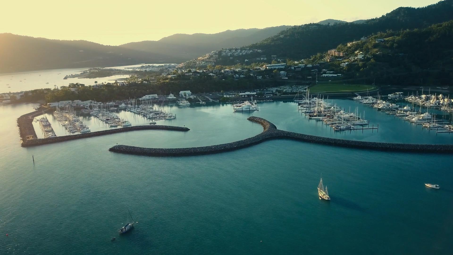 An aerial view of the Whitsundays Marina, showcasing the installation of new satellites by Air Bridge, with boats docked and clear blue waters surrounding the vibrant marina.